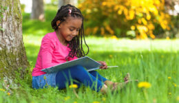 young black girl reading book under tree