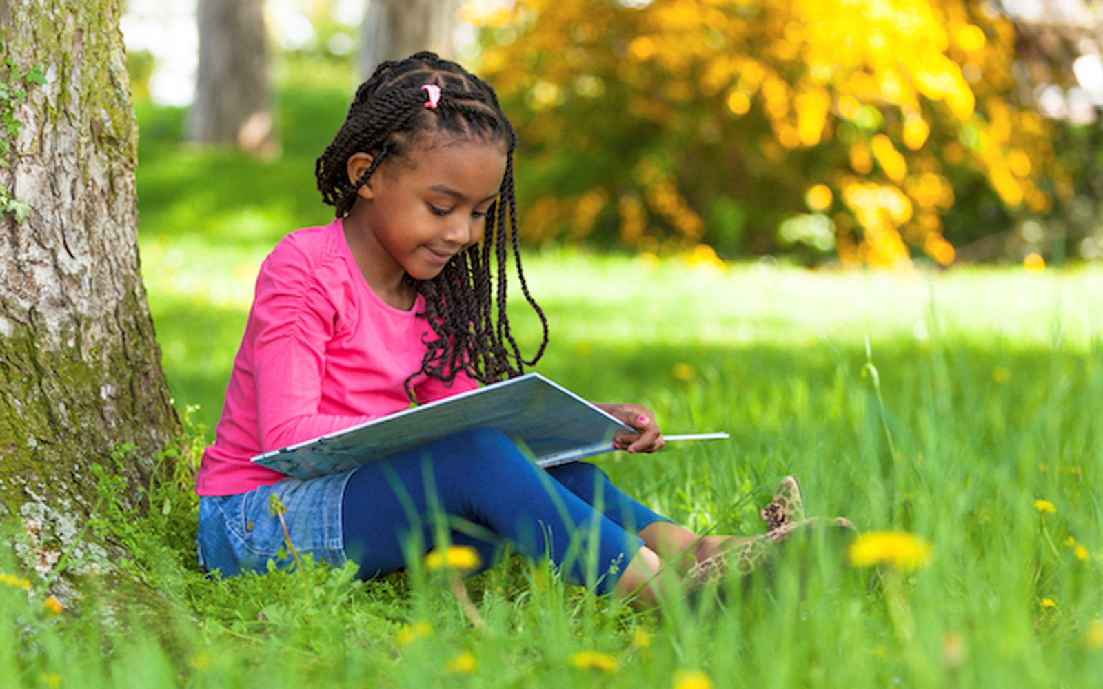 young black girl reading book under tree