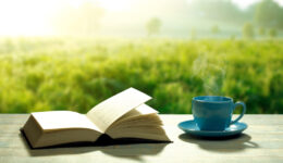 open novel book with a blue coffee cup and a wooden table