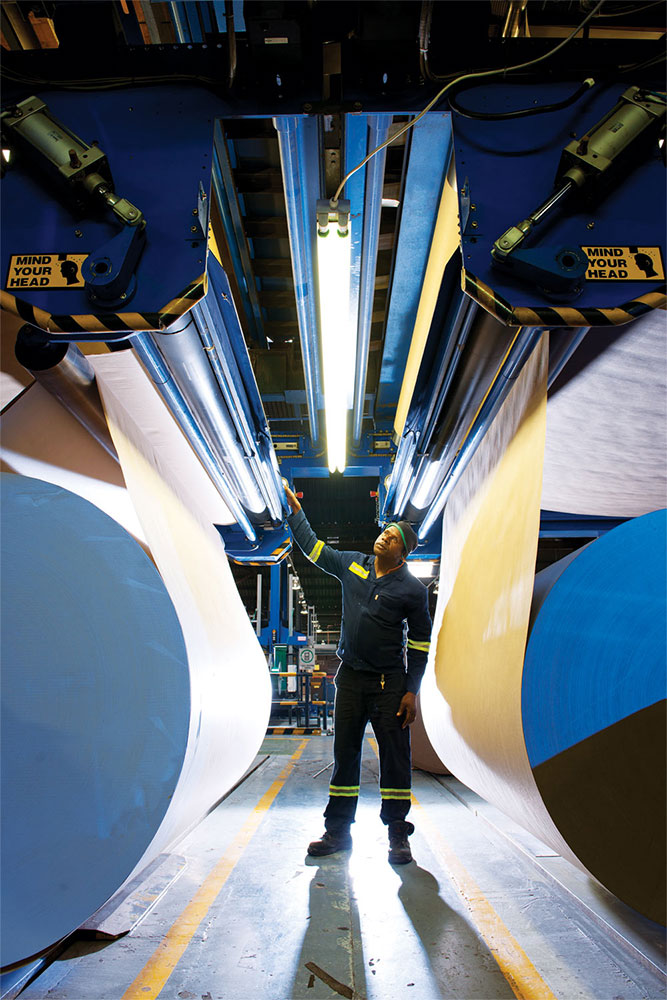 Worker standing under paper manufacturing machinery