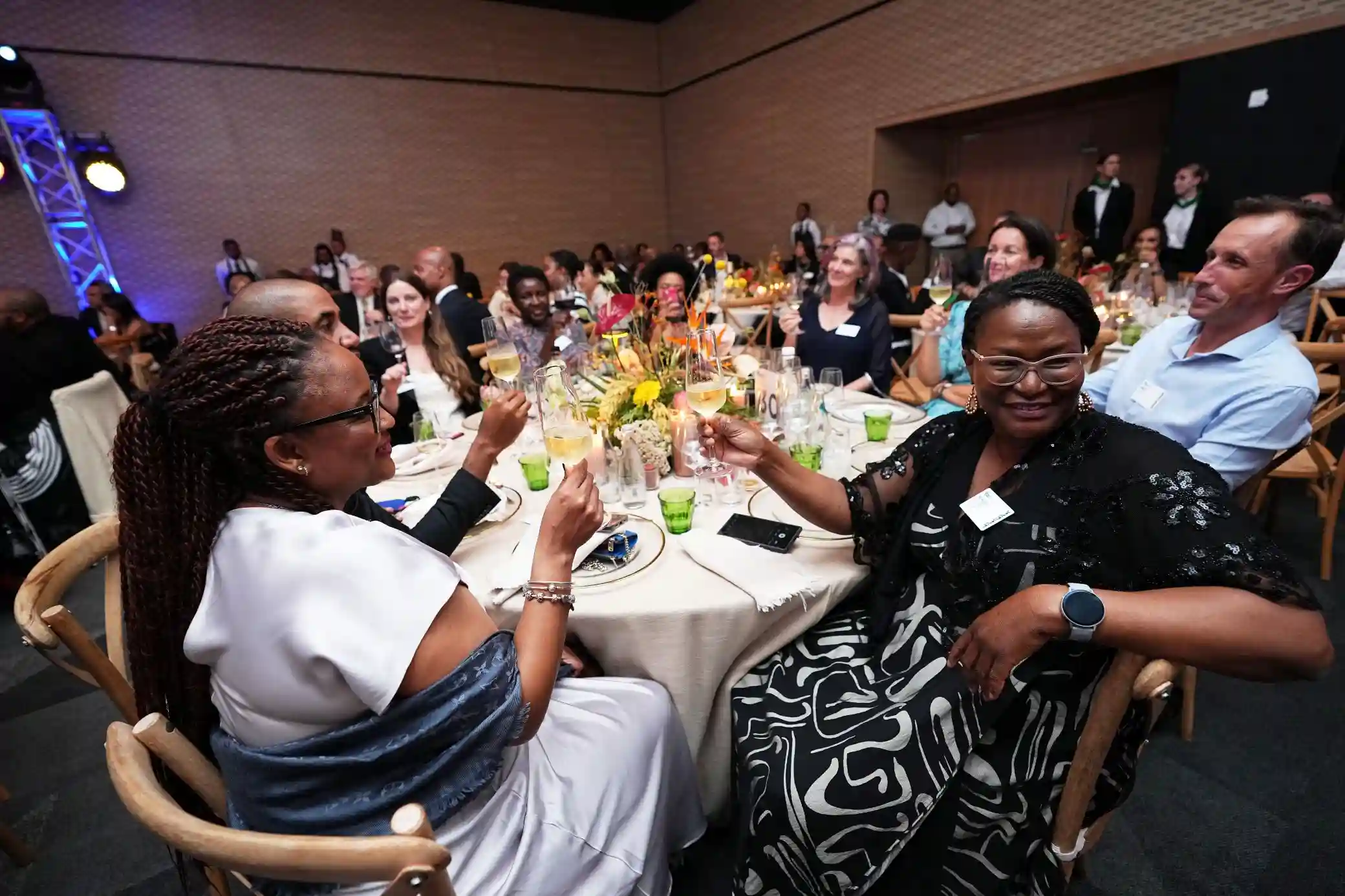 People at a formal dinner toast, raising wine glasses around a long table with flowers and candles.