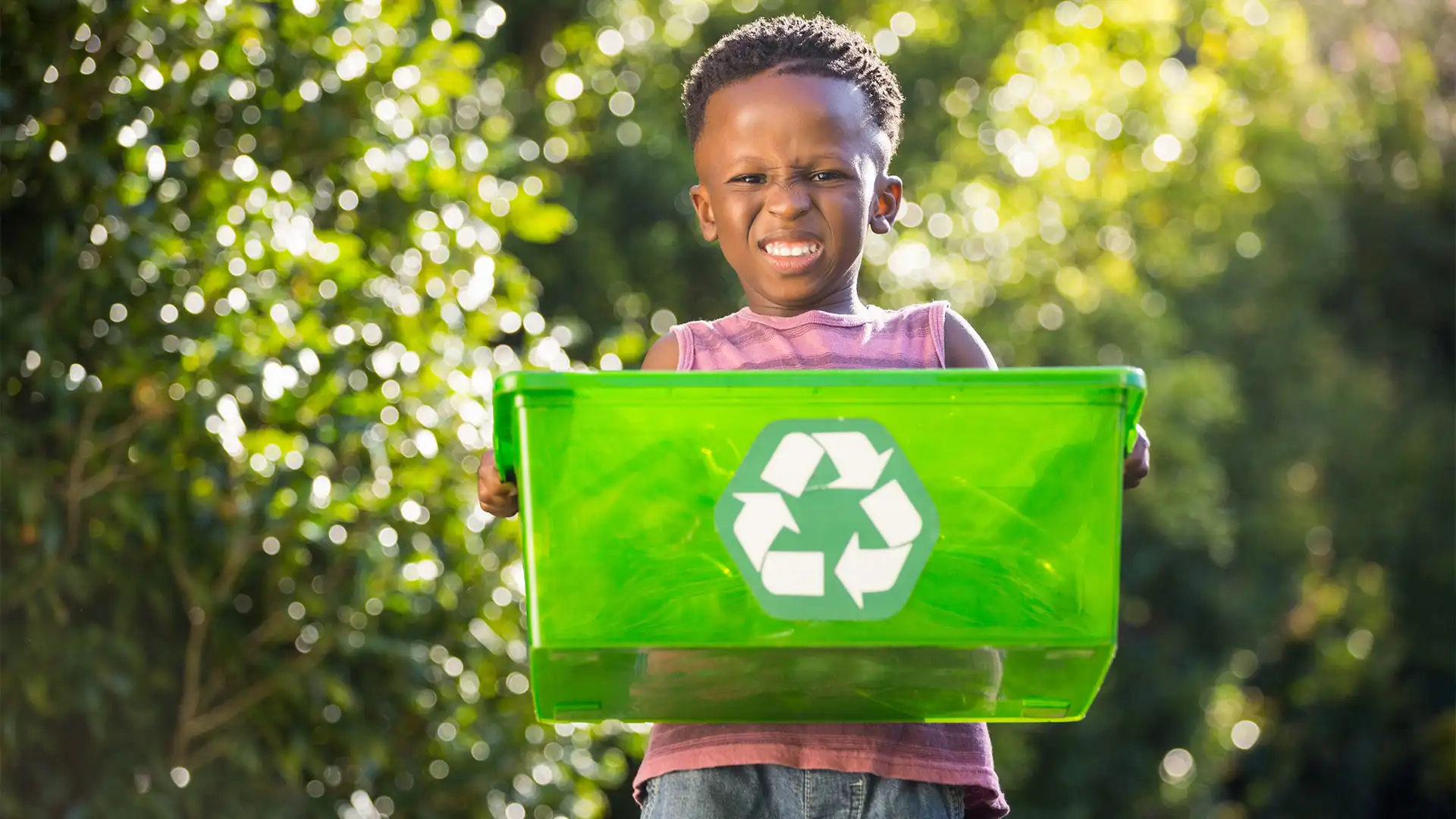 child holding green recycling bin outdoors